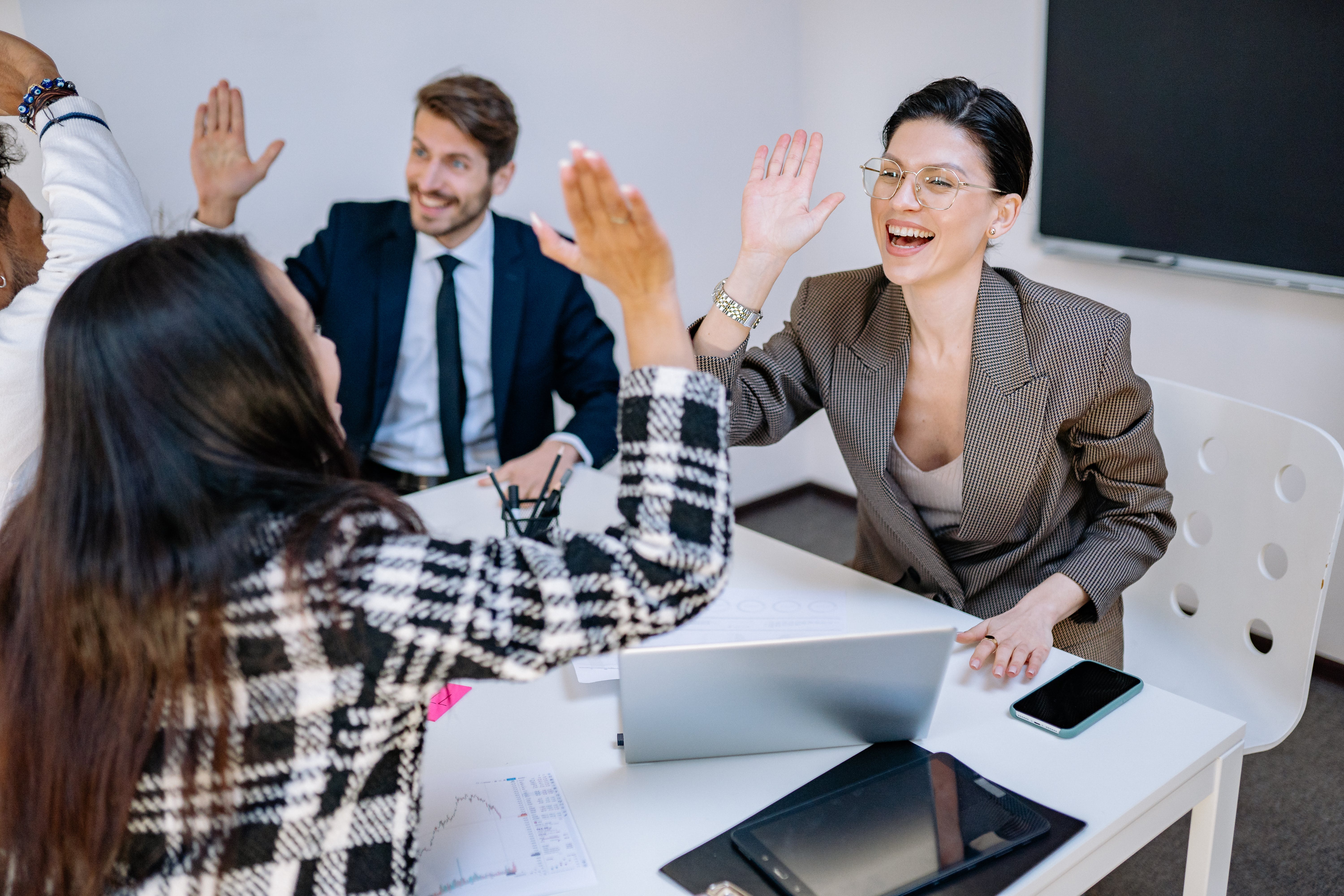 Employees sitting around a meeting table giving High fives. 